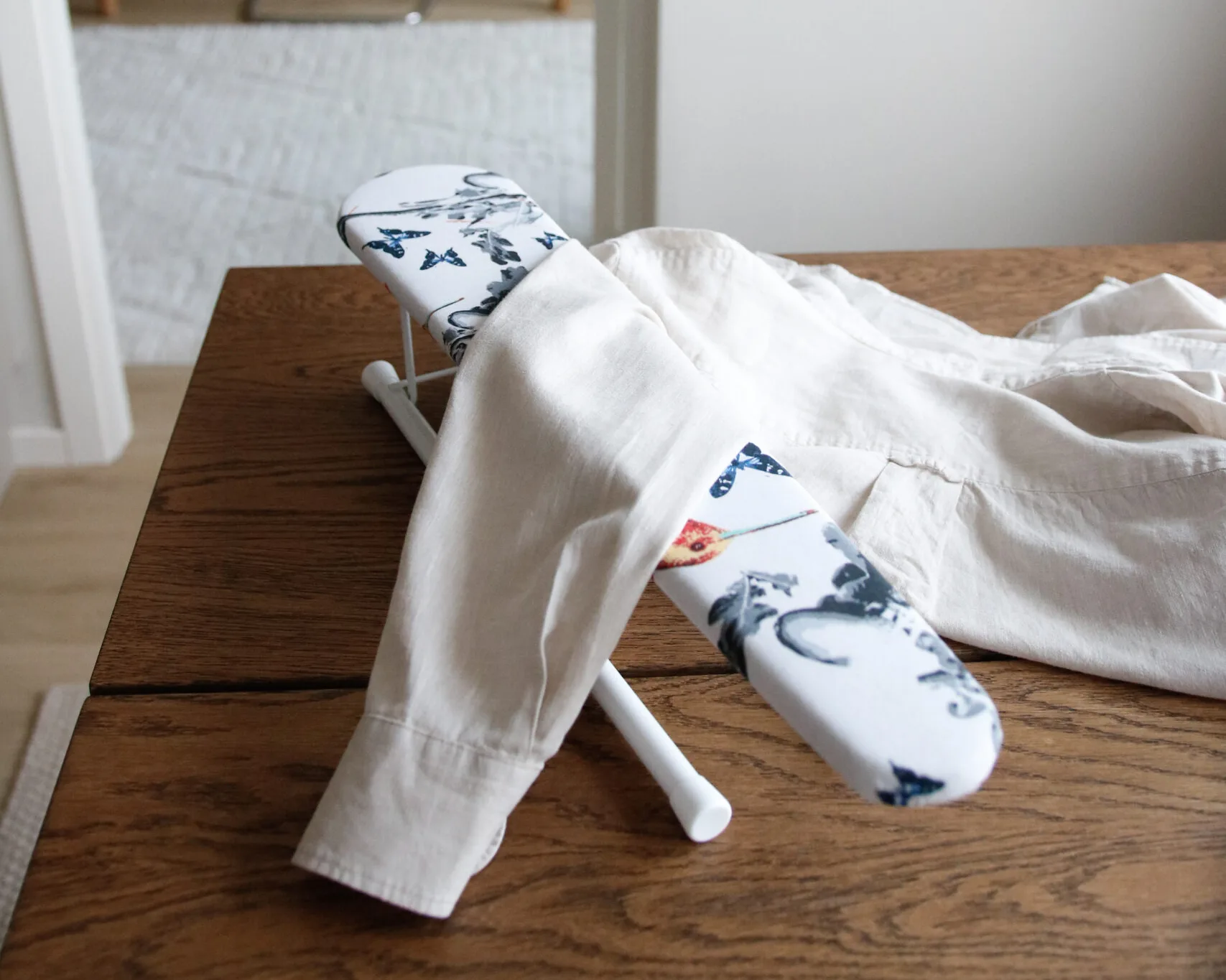 Ode liten strykbräda placerad på träbord med skjorta i ljus hemmiljö.